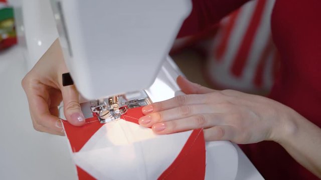 seamstress is stitching by sewing machine part of patchwork quilt, directing fabric under foot by hands