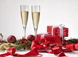 Champagne glasses, christmas decoration and two red gifts with white ribbon