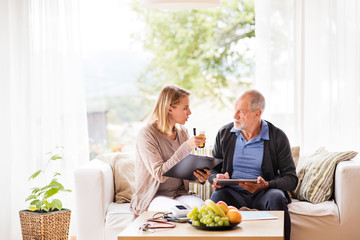 Health visitor and a senior man with tablet during home visit.