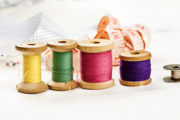 Set of tools and accessories for sewing and needlework with threads in spools, needles, measuring tape and other items on a white background