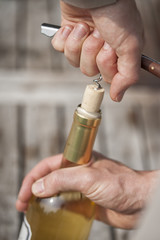 man uncorking a bottle of white wine with a corkscrew