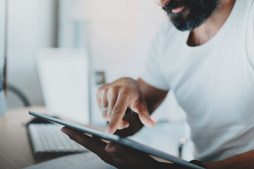 Bearded man working at the modern office loft.Coworker using electronic touch pro tablet computer at lightful workplace.Horizontal. Blurred background.