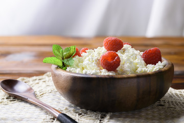Cottage cheese with fresh raspberry in a wooden bowl on old wooden background with copy space for your text. Top view