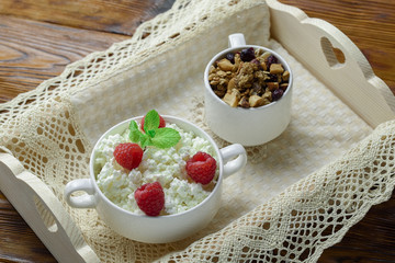 Homemade breakfast: cottage cheese with fresh raspberries and granola. In a white porcelain bowl, on a wooden tray