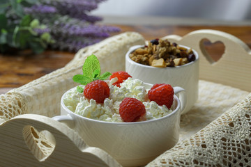 Homemade breakfast: cottage cheese with fresh raspberries and granola. In a white porcelain bowl, on a wooden tray