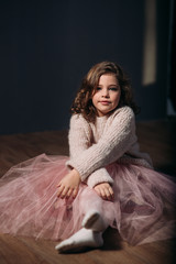 Little beautiful girl with brown hair in a light sweater and a skirt of tulle. Studio. A princess poses for a photographer.