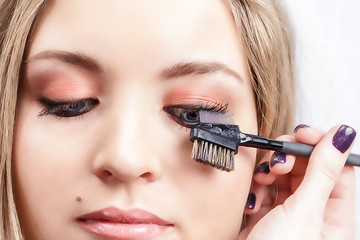 The final stage of makeup. The make-up artist combs the eyelashes of the model. Close-up