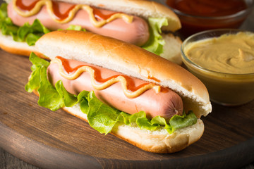 Tasty barbecue grilled hot dog with salad,yellow mustard, onion, ketchup, and French fries on wooden background. Junk and fast food concept.