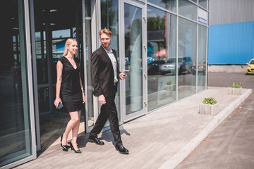 Happy couple buying new car walking from vehicle salon. Man and woman ownres of new electro car.