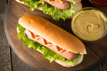 Tasty barbecue grilled hot dog with salad,yellow mustard, onion, ketchup, and French fries on wooden background. Junk and fast food concept.