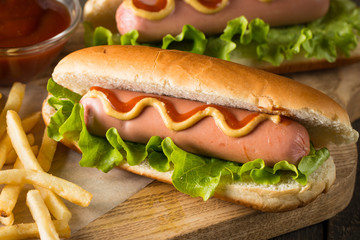 Tasty barbecue grilled hot dog with salad,yellow mustard, onion, ketchup, and French fries on wooden background. Junk and fast food concept.