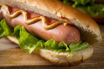 Tasty barbecue grilled hot dog with salad,yellow mustard, onion, ketchup, and French fries on wooden background. Junk and fast food concept.