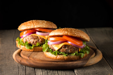 Close-up photo of home made hamburger with beer made of beef, onion, tomato, lettuce, cheese and spices. Fresh burger closeup on wooden rustic table with potato fries and chips.