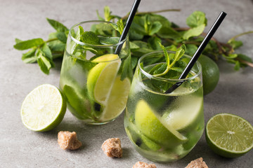 Fresh made mojito cocktail with lime, brown sugar, ice cubes and mint on a grey stone background. Alcoholic drink and lemonade concept.