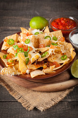 Corn Mexican nachos with beef, jalapeno, cheese, pepper, olives and chili con carne on a wooden background. Lime, Ketchup, sour cream and mayonnaise souce seasoning.