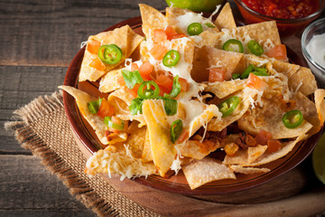 Corn Mexican nachos with beef, jalapeno, cheese, pepper, olives and chili con carne on a wooden background. Lime, Ketchup, sour cream and mayonnaise souce seasoning.