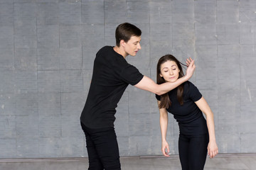 Young dancers practicing in studio. Young girl holding her head on boy hand, practicing dance element. Young skillful dancers in action.