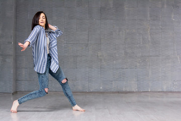 Young girl performing hip-hop dance. Young pretty woman dancing street dance on grey wall...