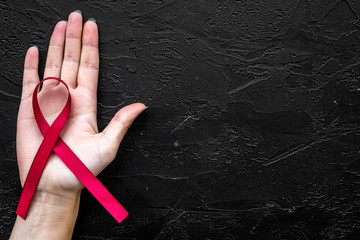 Hand hold red ribbon for HIV, AIDS, substance-abuse and anorexia awareness on black background top view copyspace