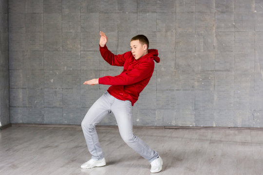 Cute young dancer posing on grey background. Caucasian teenager dancer dancing street dance on studio background.
