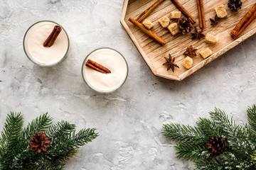 Homemade classic eggnog with cinamon and badian on wooden tray near spruce branch, pinecones on grey stone background top view