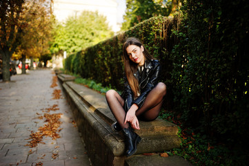 Stylish brunette girl wear on leather jacket and shorts sitting at street of autumn city.