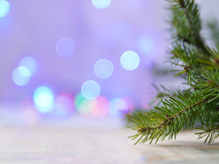 Fototapeta na wymiar New Year and Christmas background with blurred lights flare garland. Branch of spruce on a wooden surface in the foreground. Beautiful blurry colored bokeh.