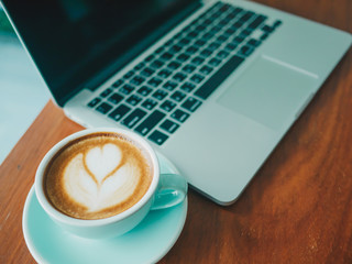 Computer laptop and heart shape coffee cup on wooden in coffee shop.