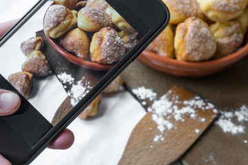 Female hand takes pictures of cottage cheese sugar cookies on mobile phone for social network pictures.