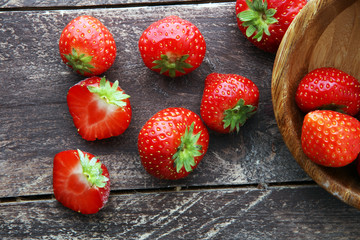 Fresh strawberries in a bowl and on a wooden background.