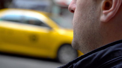 Over shoulder of young man waiting for yellow taxi cab in New York City during day time.