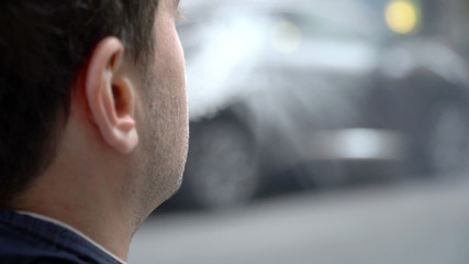 Over shoulder perspective view of young urban millennial hipster man smoking e-cig vape outside on city street. Exhale vaporized smoke created by flavored oil.