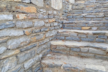 An old stone staircase among the walls of stone. Stairs made of stones of different shapes and sizes. Stone background.