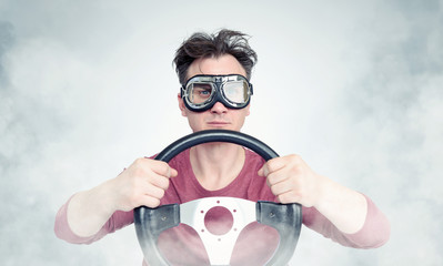 Man in stylish goggles with steering wheel on background, car driver concept