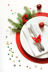 Christmas table setting with white dishware, silverware and red decorations on white background. Top view.