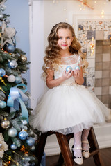 Merry Christmas celebration. Beautiful little girl in a amazing dress sitting near the Christmas...