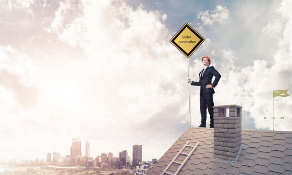 Young businessman on house brick roof holding yellow signboard a