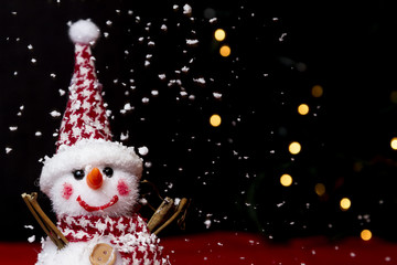 Snowman on snow over blurred christmas tree and light bokeh