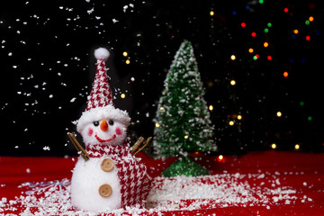 Snowman on snow over blurred christmas tree and light bokeh