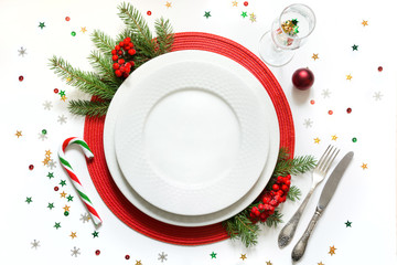 Christmas table setting with white dishware, silverware and red decorations on white background. Top view. - Powered by Adobe