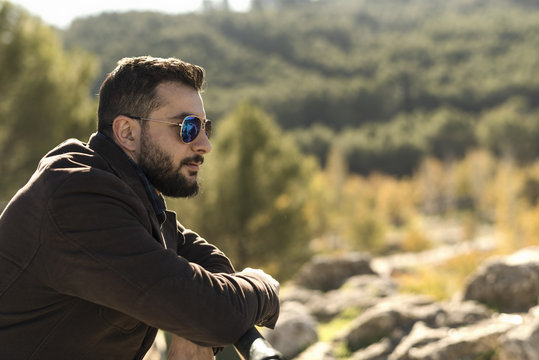 Bearded man with sunglasses supported on a railing looking tonature countryside copyspace in outdoors image