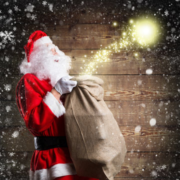 Weihnachtsmann mit Geschenkesack und Magie vor Holzhintergrund 