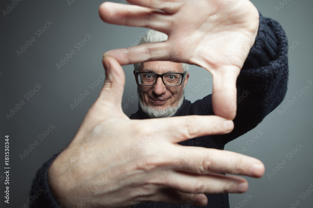 Wall mural Fabulous at any age. Eyewear concept. Portrait of a handsome mature man looking at camera through frame made of his hands. Close up. Studio shot