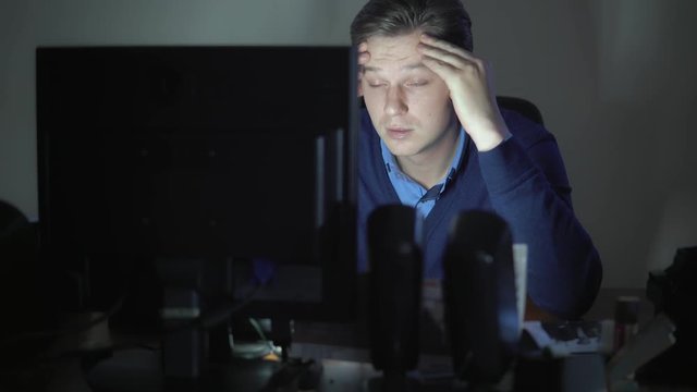 A sleepy man works at night in the office at the computer.
