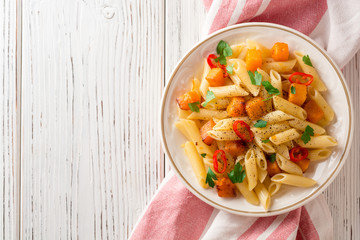 Penne pasta with pumpkin, chilli and parsley in plate on white wooden background
