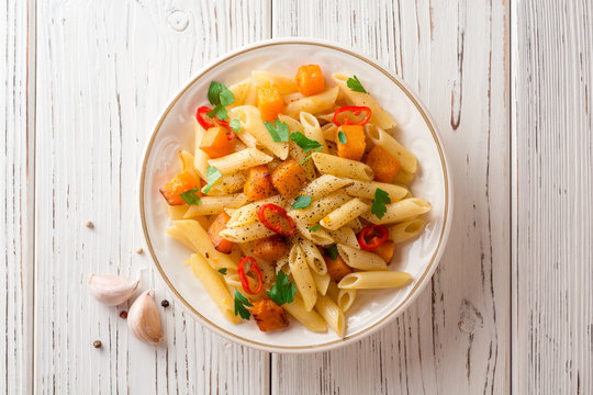 Penne pasta with pumpkin, chilli and parsley in plate on white wooden background