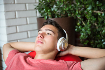 Young man, lying and enjoying with white wireless headphones, listening to music