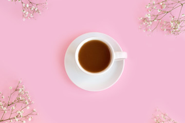 Obraz na płótnie Canvas A cup with a coffee or tea on a pink background with a white gypsophila 