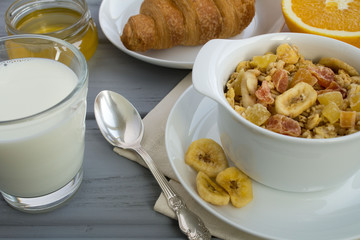 Breakfast with muesli, milk and croissant on the grey wooden background