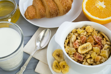 Breakfast with muesli, milk and croissant on the grey  wooden background. View from above.